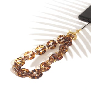 Könnte beinhalten: Eine braune und goldene Handykette mit einem Schildpattmuster. Die Kette ist aus Kunststoff und hat einen goldenen Verschluss.