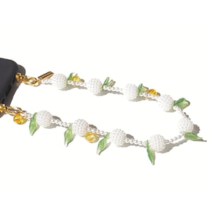 May include: A black smartphone case attached to a decorative beaded strap featuring white spherical textured beads, small white round pearls, translucent green leaf-shaped charms, and small yellow beads connected by gold-toned metal hardware.
