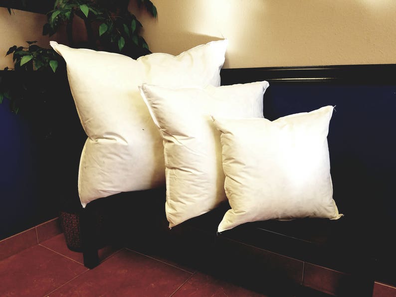 Puede incluir: Cuatro rellenos de almohada blancos de diferentes tama&ntilde;os est&aacute;n dispuestos en un sof&aacute; azul oscuro. Las almohadas est&aacute;n hechas de un material suave y esponjoso y son perfectas para agregar comodidad y estilo a cualquier habitaci&oacute;n.
