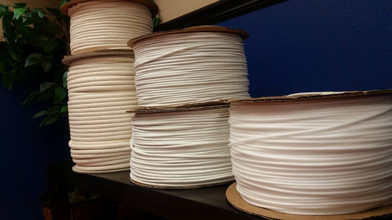 May include: Close-up of four spools of white cord or rope, stacked on a shelf. The spools are made of cardboard and have a white label.