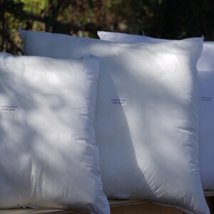May include: Four white pillows stacked on top of each other. The pillows are made of a soft, white fabric and have a smooth, even surface. The pillows are all the same size and shape.