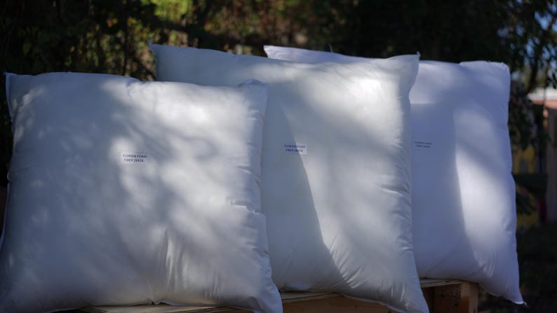 May include: Four white pillows stacked on top of each other. The pillows are made of a soft, white fabric and have a smooth, even surface. The pillows are all the same size and shape.