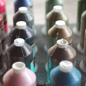 May include: A collection of spools of thread in various colors, including gold, brown, pink, blue, and green. The spools are arranged in rows on a dark surface.