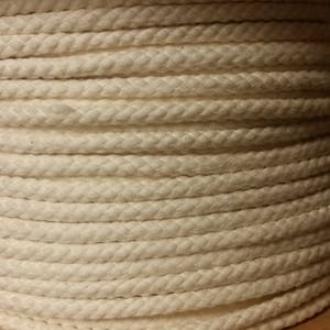 May include: A close-up of a reel of white cotton rope. The rope is tightly wound and has a smooth, even texture.