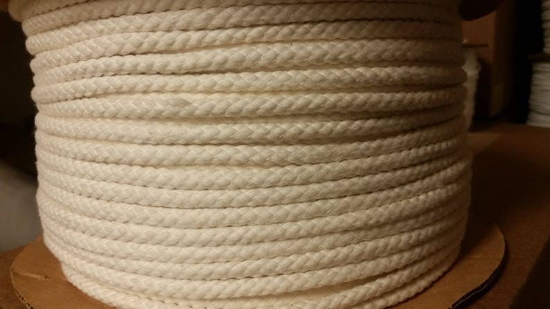 May include: A close-up of a reel of white cotton rope. The rope is tightly wound and has a smooth, even texture.