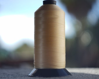 May include: A spool of cream-colored thread with a black plastic base.