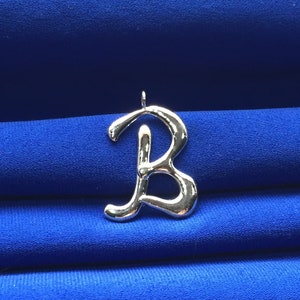 May include: A silver-coloured letter B charm pendant. The letter is stylised and has a smooth, shiny finish. The pendant is on a blue background.