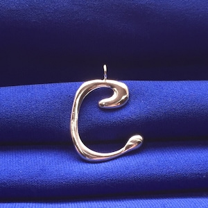 May include: A silver-coloured pendant shaped like the letter C. The pendant is on a blue background.