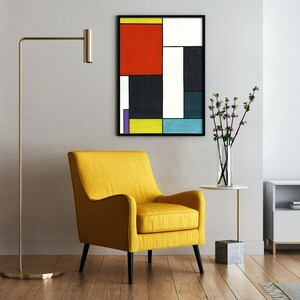 May include: A yellow armchair with black legs sits in front of a geometric abstract painting with red, yellow, blue, black, and white squares. A vase with pink flowers and a small side table are to the right of the chair.