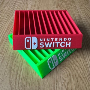 May include: Two stackable game cartridge storage cases, one red and one green, with the Nintendo Switch logo and text on the front.