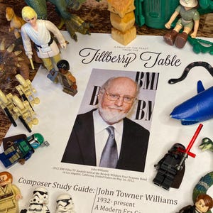 May include: A collection of toys and figurines, including dinosaurs, Lego figures, and toy soldiers, are arranged around a printed page featuring a photo of John Williams and the text "Composer Study Guide: John Towner Williams."