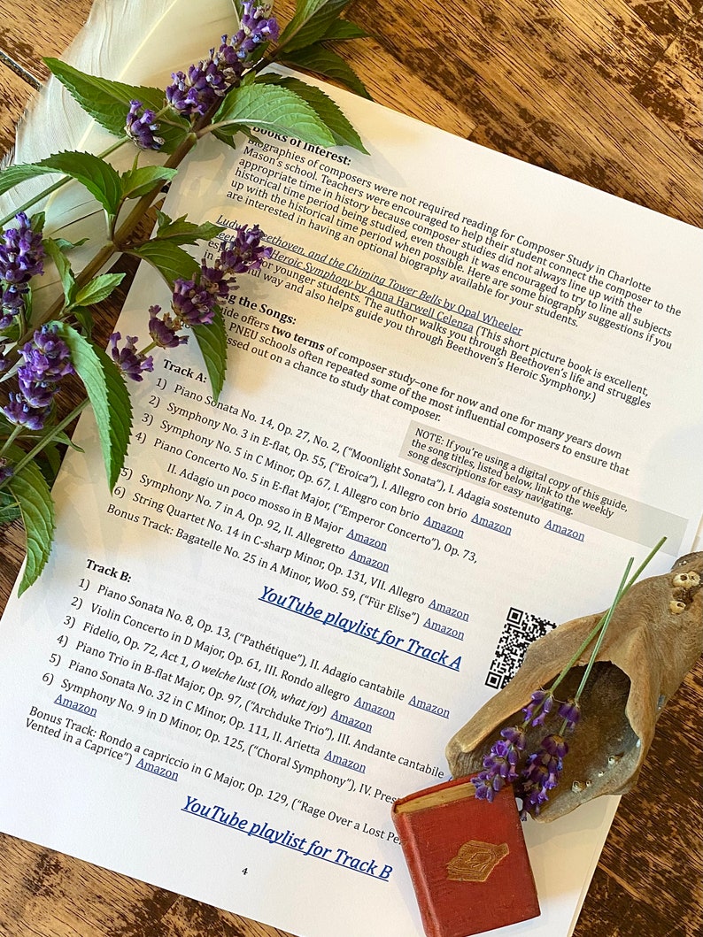 May include: A close-up of a printed sheet of paper with a list of classical music pieces, including composers and their works. The paper is on a wooden table with a small book and a decorative seashell with lavender flowers.