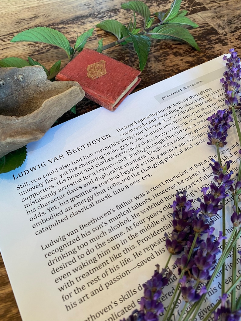 May include: A close-up of a page from a book about Ludwig van Beethoven. The text discusses his life and musical career. The page is decorated with a sprig of lavender flowers.