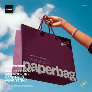 May include: A deep purple paper shopping bag mockup held against a bright blue sky. The bag has a rope handle and the word "paperbag" is prominently displayed. The text "MOCKUPS & BRANDING" is also visible.