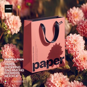May include: A pink paper shopping bag with black handles and the word "paper" printed on the front. The bag is surrounded by pink flowers and green foliage. The image also includes the text "branding drops" and "MOCKUPS & BRANDING".