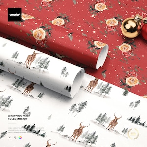 Puede incluir: Una maqueta de rollos de papel de regalo. Un rollo presenta un fondo rojo con motivos florales y detalles dorados. El otro rollo muestra una escena invernal con ciervos y árboles. La imagen también incluye adornos navideños.
