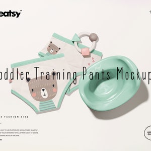 May include: Two pairs of toddler training pants with a bear print design. The pants are white with green trim and a brown bear with a pink nose and green stripes. The pants are laid out on a white surface with a small green bowl and a pink and grey toy.