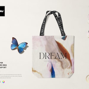 May include: A white canvas tote bag mockup with black straps and the word "DREAM" printed on the front. The bag has a watercolour-like design with shades of pink, blue, and brown. The straps have the text "A DREAM YOU DEP" and "ONE IS ONLY A DREAM" printed on them.