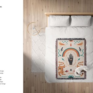 K&ouml;nnte beinhalten: Ein wei&szlig;es Bett mit einer bunten gewebten Wolldecke mit einem Regenbogen, einer Hand mit einem Auge und einer Schlange. Die Decke hat einen Fransenrand. Das Bett steht auf einem Holzboden mit einem wei&szlig;en Teppich.
