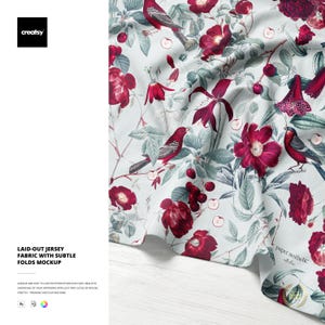 May include: Jersey fabric mockup with a floral and bird pattern. The fabric features red flowers, birds, and cherries on a light background. The text "LAID-OUT JERSEY FABRIC WITH SUBTLE FOLDS MOCKUP" is visible.
