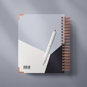 Op de afbeelding: Een wit spiraalnotitieblok met een geometrisch ontwerp in zwart, wit en grijs. Het notitieblok heeft een koperkleurige binding en een witte pen ligt erop.