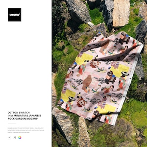 May include: A cotton swatch with a Japanese-themed design, featuring figures and animals in various colors on a pink background. The swatch is displayed on a miniature rock garden with green moss and stones. The text "COTTON SWATCH IN A MINIATURE JAPANESE ROCK GARDEN MOCKUP" is visible.