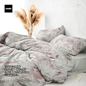 Può includere: Mockup di copripiumino e federe stropicciate con un motivo floreale nei toni del rosa e del grigio. La biancheria da letto è disposta su un letto con un lenzuolo bianco. L'immagine include il testo "WRINKLED DUVET COVER & PILLOWCASES MOCKUP".