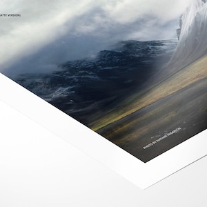 May include: A close-up of a matte photo print of a mountain range with a cloudy sky. The photo is framed with a white mat and a white border. The text "PHOTO BY NATASHA INGARDSON" is printed in the bottom right corner.