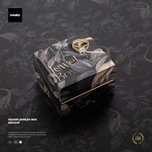 May include: A gold ring with a large, clear gemstone sits atop a black square jewelry box. The box is decorated with a floral pattern in shades of gray and gold, with the words "Jewel Box" in gold lettering. The background is a dark floral pattern.