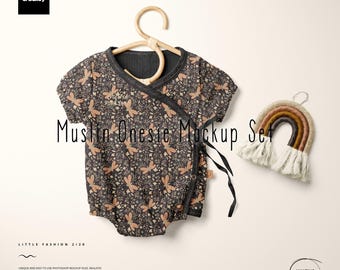 May include: A dark gray muslin onesie with a floral and dragonfly pattern, hanging on a wooden hanger. A small, rainbow-colored wall hanging with fringe is next to the onesie. The text "Muslin Onesie Mockup Set" is displayed.