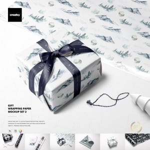 May include: A wrapped gift box with a navy blue ribbon and a matching wrapping paper. The paper features a watercolor design of mountains and trees. The ribbon has the word "WALA" printed on it.