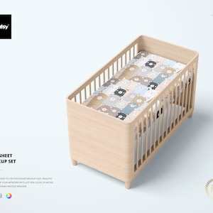 May include: A wooden crib with a white crib sheet featuring a pattern of brown, blue, and gray bears. The crib is on a white background.