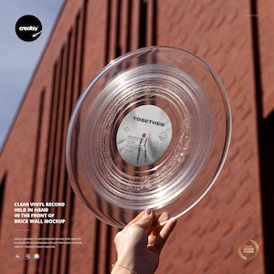 Peut inclure: Un disque vinyle transparent avec le mot "TOGETHER" sur l'étiquette. Le disque est tenu devant un mur de briques. L'image comprend également le texte "CLEAR VINYL RECORD HELD IN HAND IN THE FRONT OF BRICK WALL MOCKUP".