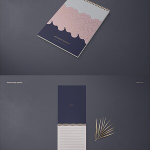 May include: A mockup of a spiral bound notebook with a navy blue cover and a pink and gold geometric pattern. The notebook is lying flat on a gray surface. The text "NOTEBOOK MOCKUP" is printed on the cover.