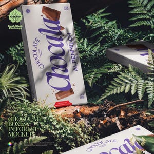 May include: White chocolate box with purple text reading "Chocolats" and "Alpenmilch" against a forest backdrop. The box features a chocolate bar graphic and the text "Pure Alpine Milk". The box is surrounded by green foliage.