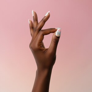 May include: A dark hand with long, white, oval-shaped nails. The thumb and index finger are touching, forming a circle. The background is a gradient of pink and peach.