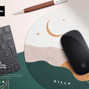 Pode incluir: Um rato sem fios preto com o logótipo da Apple repousa sobre um tapete de rato redondo. O tapete apresenta um design de paisagem com uma lua crescente e estrelas. Uma caneta castanha e um teclado preto também são visíveis. O texto "ROUND MOUSE PAD MOCKUP SET" é exibido.