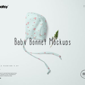 May include: A light blue baby bonnet with a pink floral pattern and white ties. The bonnet is lying on a white surface with a sprig of greenery.