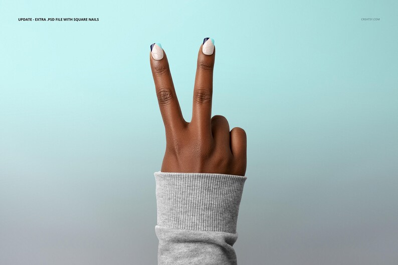May include: A hand with dark skin showing the peace sign, index and middle fingers raised. The square nails have a white base, navy blue tips, and a light blue accent. The wrist is covered by a grey ribbed sleeve. The background is a gradient.