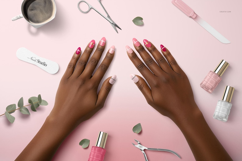 May include: Overhead view of hands with pink and red manicured nails, surrounded by nail polish, clippers, scissors, and a file on a pink surface. A cup of coffee and a nail file with "Nail Studio" text are also visible. The scene suggests a nail care theme.