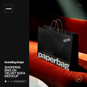 Puede incluir: Una bolsa de compras de papel negro con asas marrones descansa sobre un sofá de terciopelo rojo. La bolsa tiene la palabra "paperbag" impresa en blanco, y el logotipo "creatsy" es visible. La imagen es una maqueta para branding.