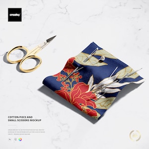 May include: A gold-colored pair of small scissors next to a blue cotton fabric with a red floral design. Several silver pins are placed on the fabric. The image includes the text "COTTON PIECE AND SMALL SCISSORS MOCKUP".