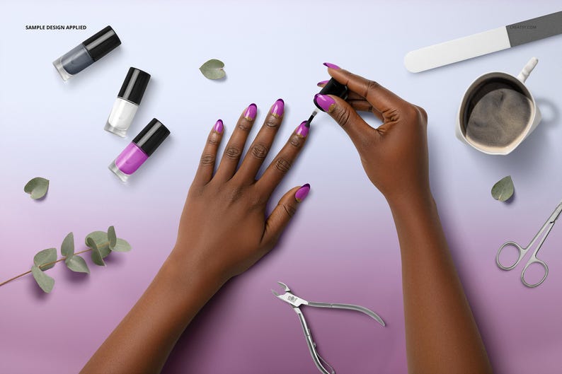 May include: A person is applying purple nail polish to their nails. The image shows a manicure in progress, with various nail polish bottles in grey, white, and purple. Manicure tools, a cup of coffee, and greenery are also visible. The nails have a purple tip.