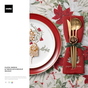 Könnte beinhalten: Eine festliche Tischdekoration mit einem rot umrandeten Teller mit Lebkuchen-Design, goldenem Besteck und einer roten Serviette. Die Serviette hält eine goldene Gabel, ein Messer und einen Löffel, die mit einem grünen Band und einem Tannenzapfen gebunden sind. Die Tischdecke hat ein Blumenmuster.