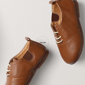 Op de afbeelding: Twee bruine leren veterschoenen met witte veters. De schoenen liggen op een wit oppervlak.