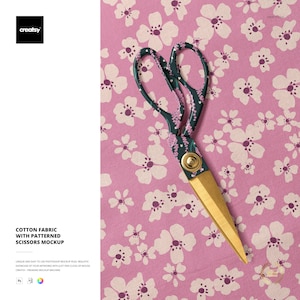 May include: Scissors with a patterned design and gold blades rest on a pink floral fabric. The scissors have a dark green handle with a floral pattern. The text "COTTON FABRIC WITH PATTERNED SCISSORS MOCKUP" is visible.