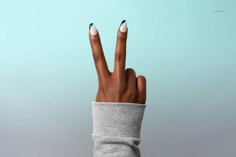 May include: A hand displaying a peace sign, with two fingers raised. The nails are decorated with a white, black, and blue design. The wrist is covered by a grey ribbed sleeve, against a gradient blue backdrop.