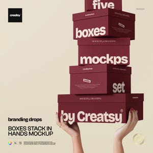 Op de afbeelding: Een stapel van vijf bordeauxrode dozen met witte tekst, waaronder "boxes", "mockups" en "set". De dozen worden door handen vastgehouden, met de tekst "by Creatsy" onderaan. De afbeelding bevat ook de tekst "BOXES STACK IN HANDS MOCKUP."
