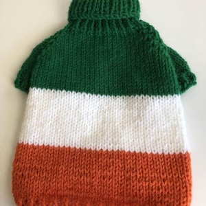 May include: A knitted dog sweater in the colors of the Irish flag: green, white, and orange. The sweater has a turtleneck collar and short sleeves. The garment is made of a thick yarn.
