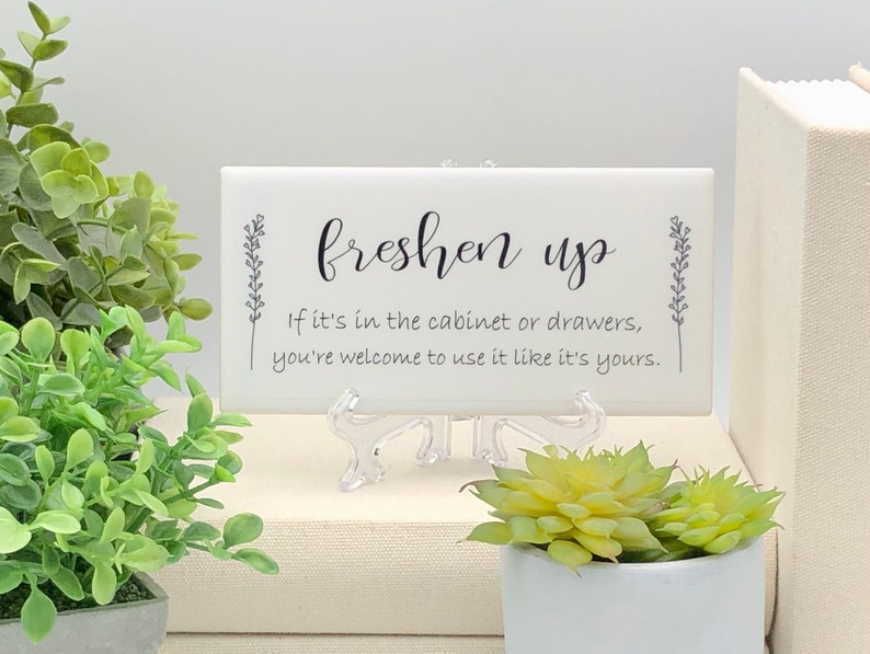 May include: White ceramic sign with black text that reads "freshen up" and "If it's in the cabinet or drawers, you're welcome to use it like it's yours."